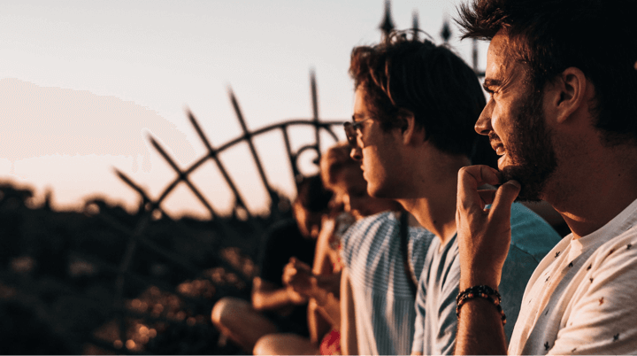 Group of males sat on a wall looking into a sunset